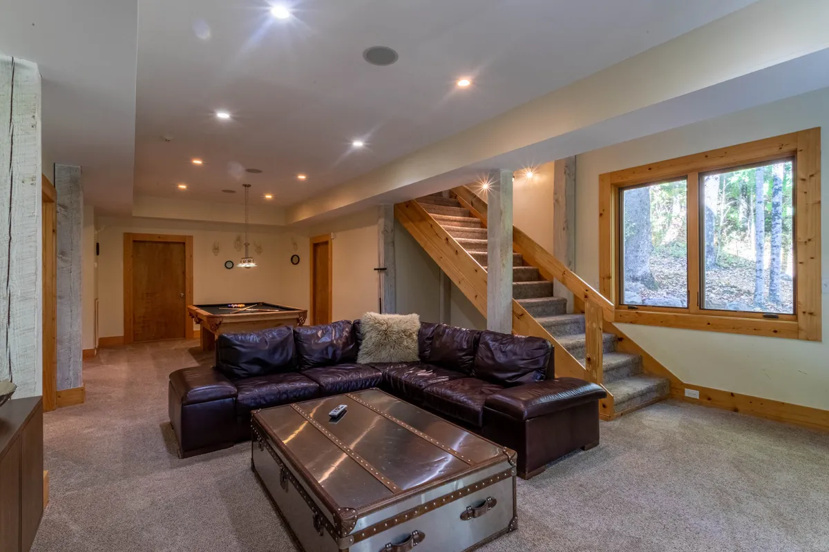 This image features a relaxed interior den with a leather sectional sofa, a pool table, and a staircase. The atmosphere is casual and inviting, with space for both socializing and friendly billiards games. Intimate gatherings and relaxed afternoons are clearly encouraged by the room's setup.
