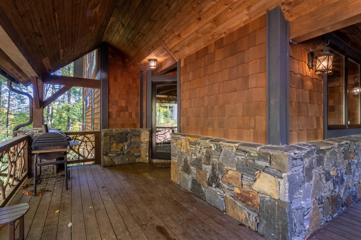 This exterior image showcases a cozy wooden deck with a stone wall, lantern lighting, and easy indoor-outdoor access via a glass door. The setting is perfect for enjoying sunset views, socializing, or relaxing with a drink after exploring local attractions.