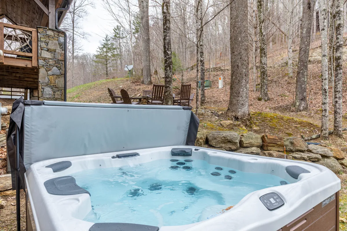 This image presents a tranquil exterior space with a private hot tub surrounded by trees and an inviting outdoor seating area. The hot tub is positioned for privacy and offers an immersive experience in nature, ideally suited for romantic stargazing or peaceful morning relaxation.