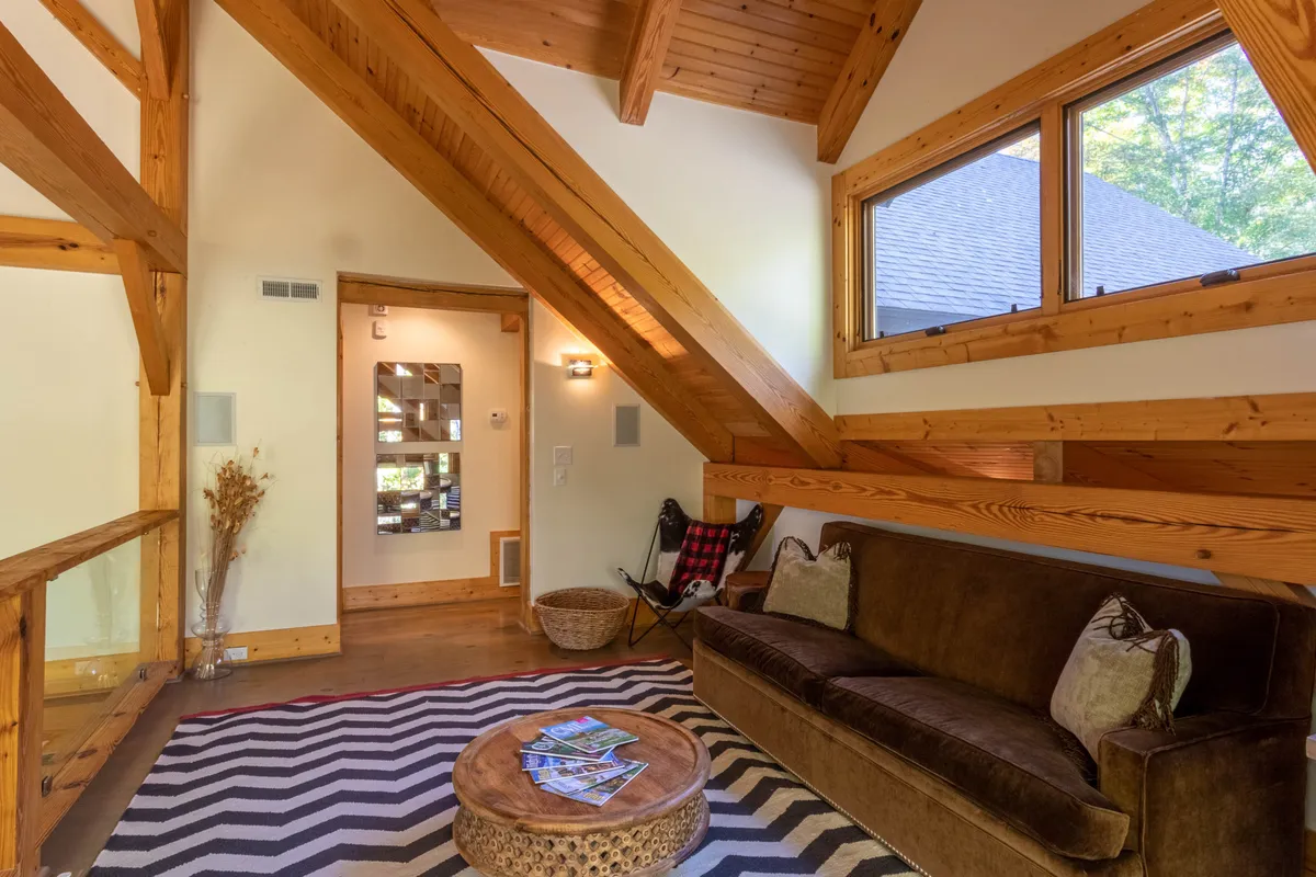 A bright, inviting living room featuring wooden beams, a comfortable sofa, a coffee table, and large windows that let in natural light. The space feels open and connected to the outdoors, suggesting a perfect place to relax after a day exploring Banner Elk and beyond.
