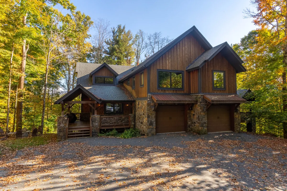 The exterior of a welcoming townhome, featuring a wooden facade, stone accents, large windows, and a driveway surrounded by trees. The environment is serene and inviting, perfect for family gatherings, nature walks, and relaxing on the porch.