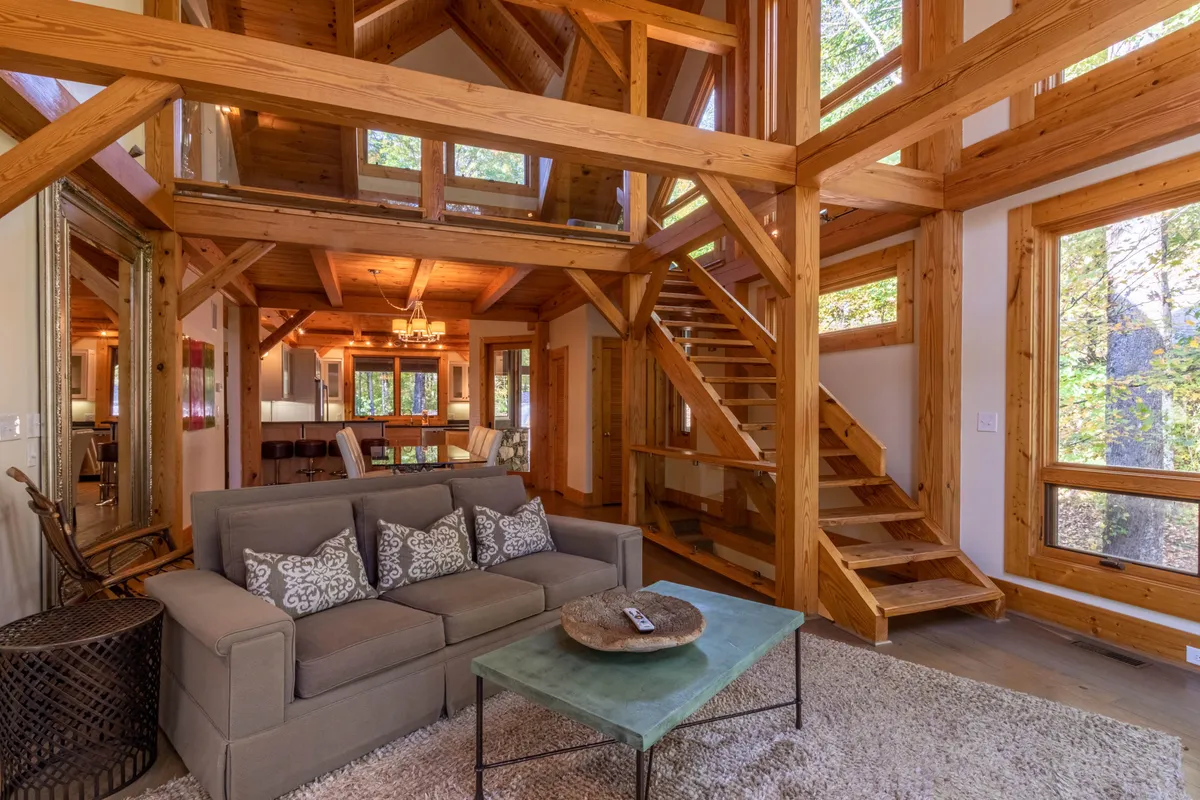 A cozy interior living area with a comfortable sofa, coffee table, staircase, and large windows letting in sunlight. The space feels welcoming and warm, ideal for relaxing after outdoor activities or quality time with family and pets.