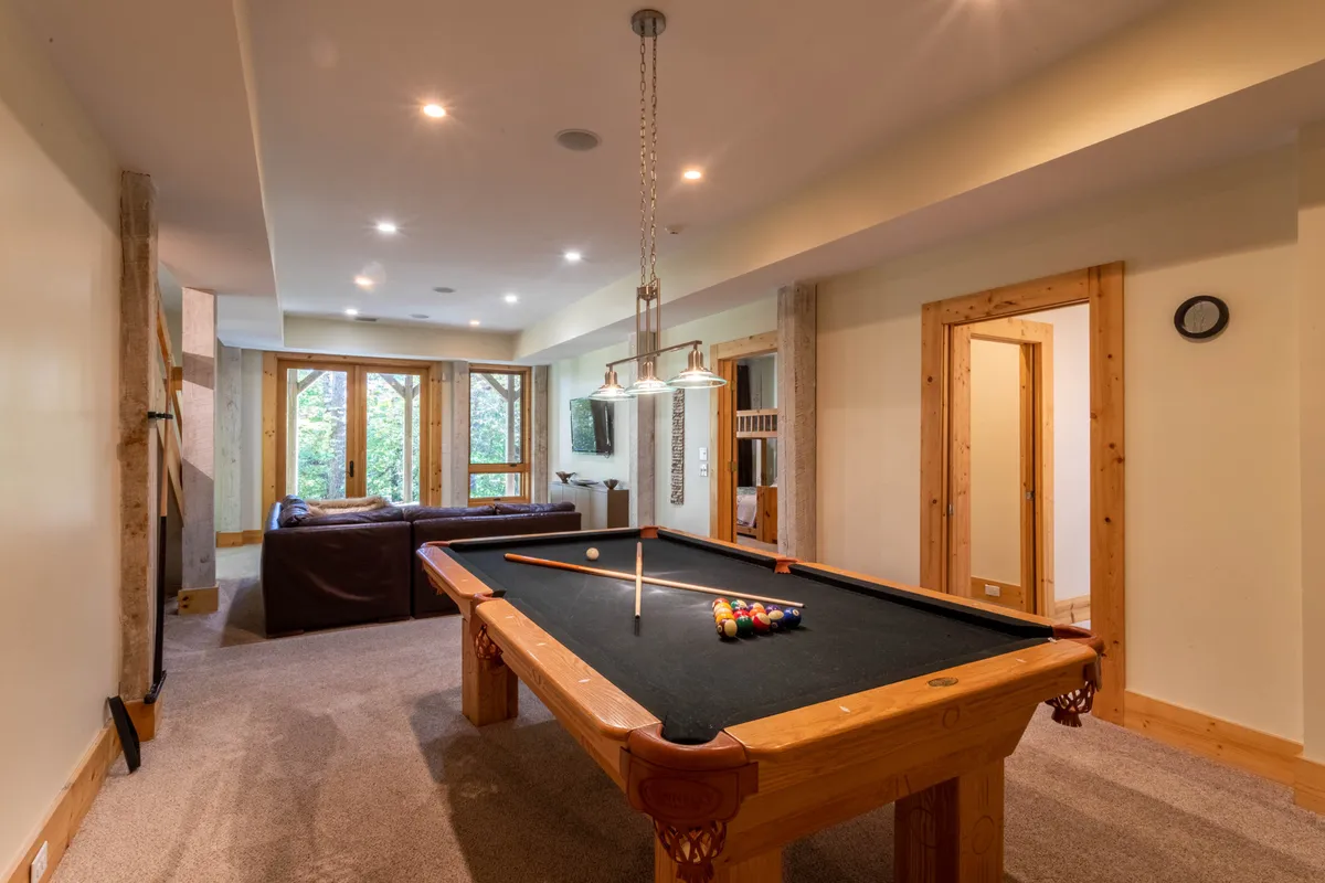 This interior shot presents a pool table, a sofa, large windows, and a TV, creating a space designed for both playing billiards and unwinding while watching movies or enjoying the view. It's a casual, friendly environment that highlights multiple entertainment options.