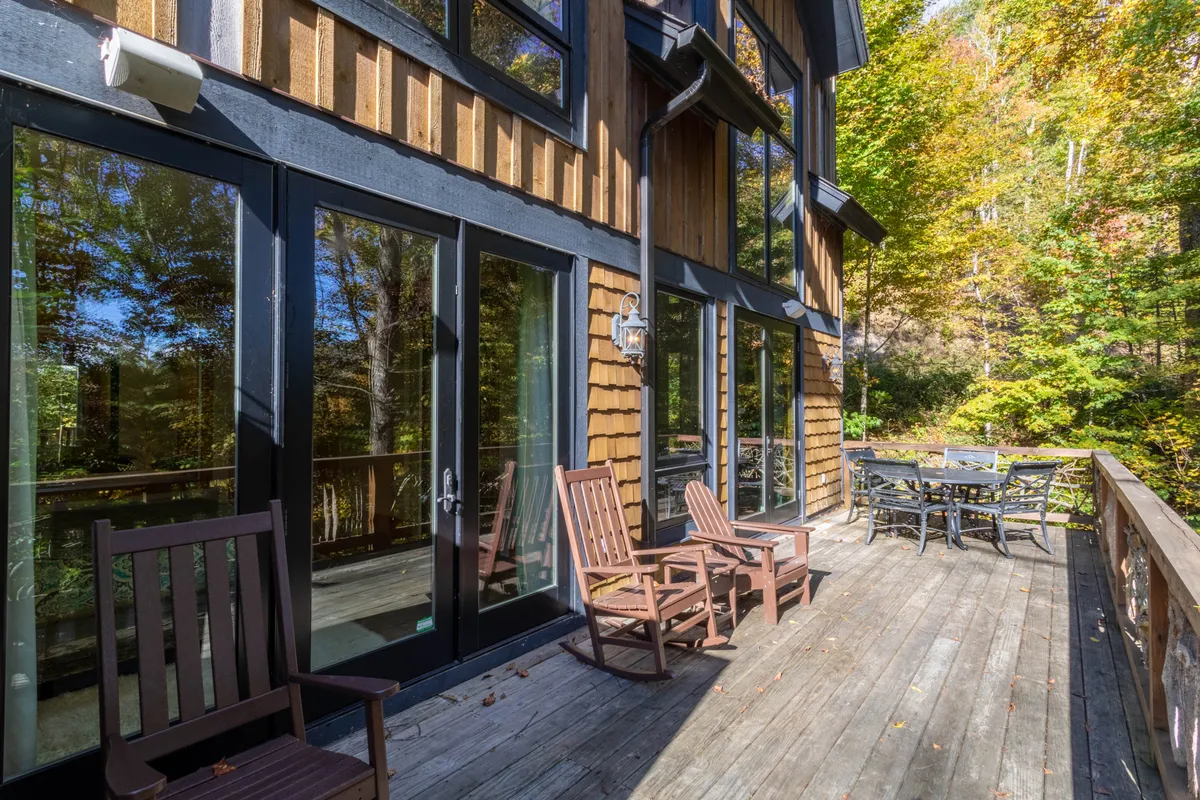 A tranquil wooden deck with comfortable rocking chairs and an outdoor dining table surrounded by trees. The view extends outward, offering a peaceful spot for morning coffee or sunset gatherings, directly connected to interior living spaces.